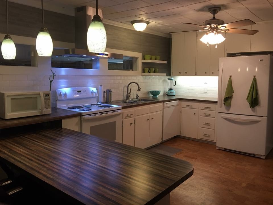 Example of a mid-sized transitional u-shaped vinyl floor and brown floor kitchen design with a drop-in sink, flat-panel cabinets, white cabinets, laminate countertops, white backsplash, subway tile backsplash, white appliances, no island and brown countertops