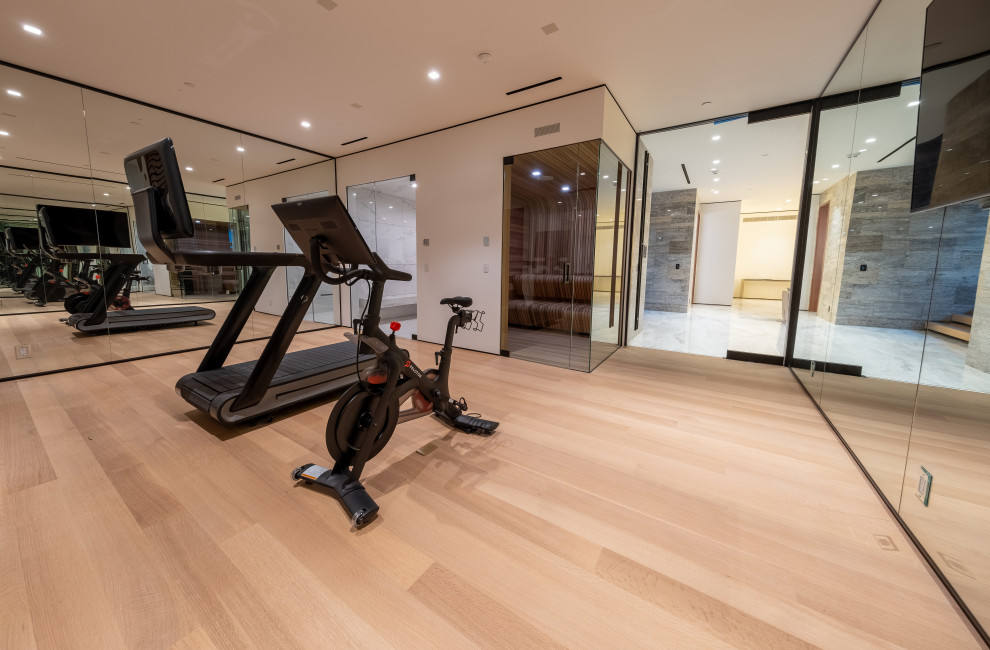 Large home weight room in Los Angeles with white walls, medium hardwood floors and brown floor.