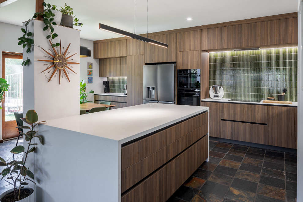 Inspiration for a mid-sized midcentury open plan kitchen in Perth with an undermount sink, medium wood cabinets, quartz benchtops, green splashback, stone tile splashback, black appliances, slate floors, with island, multi-coloured floor and white benchtop.