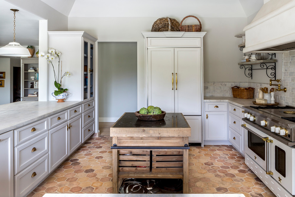 Photo of a mediterranean u-shaped enclosed kitchen in San Diego with recessed-panel cabinets, white cabinets, marble worktops, grey splashback, stone tiled splashback, white appliances, terracotta flooring, an island and beige floors.