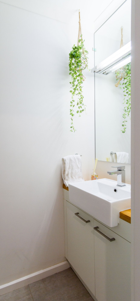 This is an example of a small modern powder room in Melbourne with flat-panel cabinets, white cabinets, white walls, porcelain floors, a drop-in sink, wood benchtops, grey floor and brown benchtops.