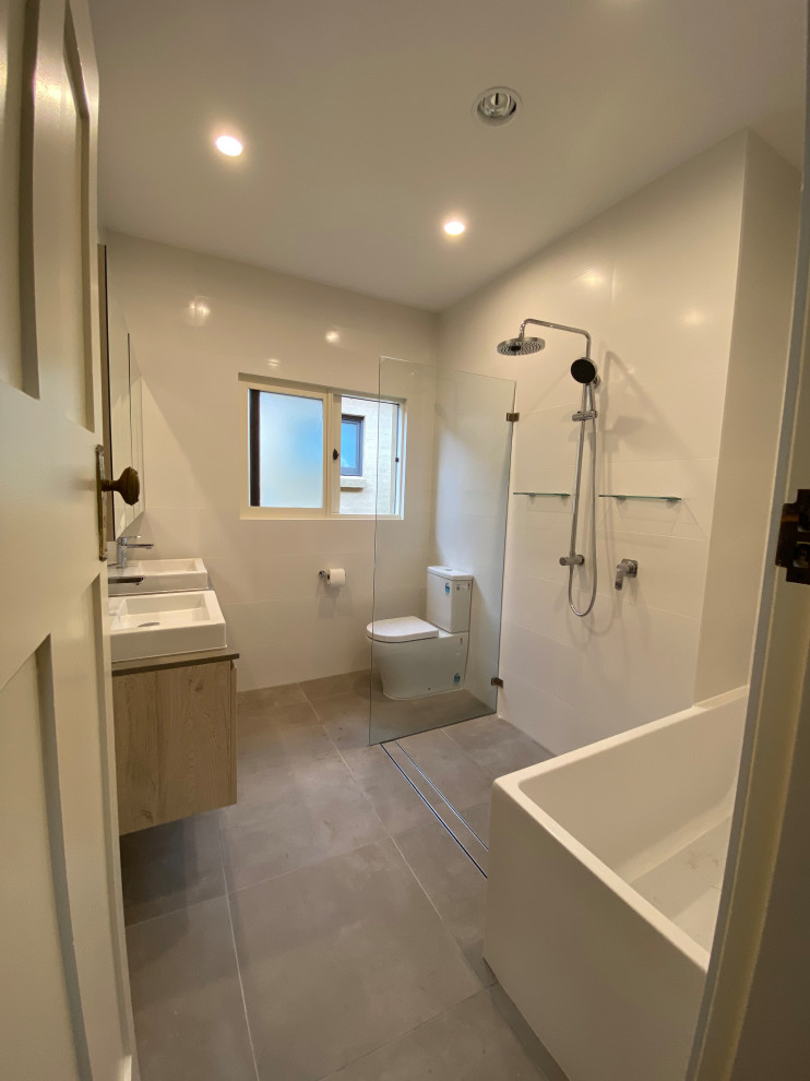 This is an example of a small contemporary master wet room bathroom in Sydney with furniture-like cabinets, grey cabinets, a corner tub, a one-piece toilet, white tile, porcelain tile, white walls, porcelain floors, a vessel sink, engineered quartz benchtops, grey floor, an open shower, grey benchtops, a niche, a double vanity, a floating vanity, recessed and brick walls.