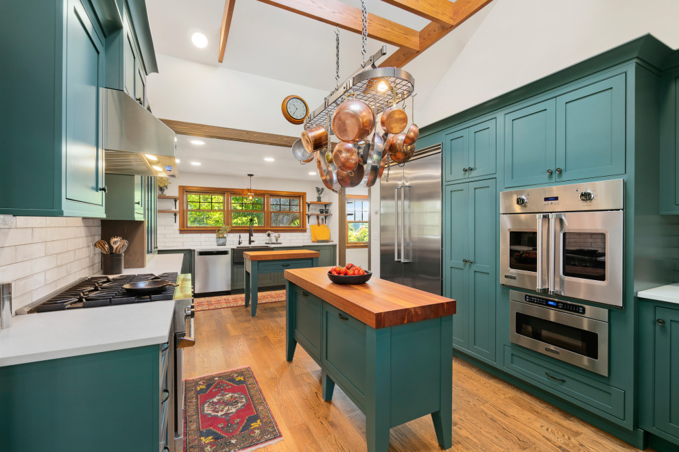 Example of a large country l-shaped medium tone wood floor, brown floor and exposed beam enclosed kitchen design in Providence with a farmhouse sink, shaker cabinets, green cabinets, quartzite countertops, white backsplash, ceramic backsplash, stainless steel appliances, two islands and white countertops