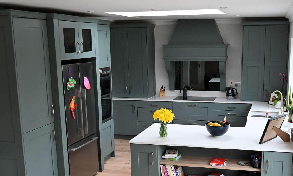 Design ideas for a mid-sized contemporary u-shaped eat-in kitchen in Dublin with a farmhouse sink, recessed-panel cabinets, green cabinets, marble benchtops, white splashback, marble splashback, stainless steel appliances, light hardwood floors, a peninsula, brown floor and white benchtop.