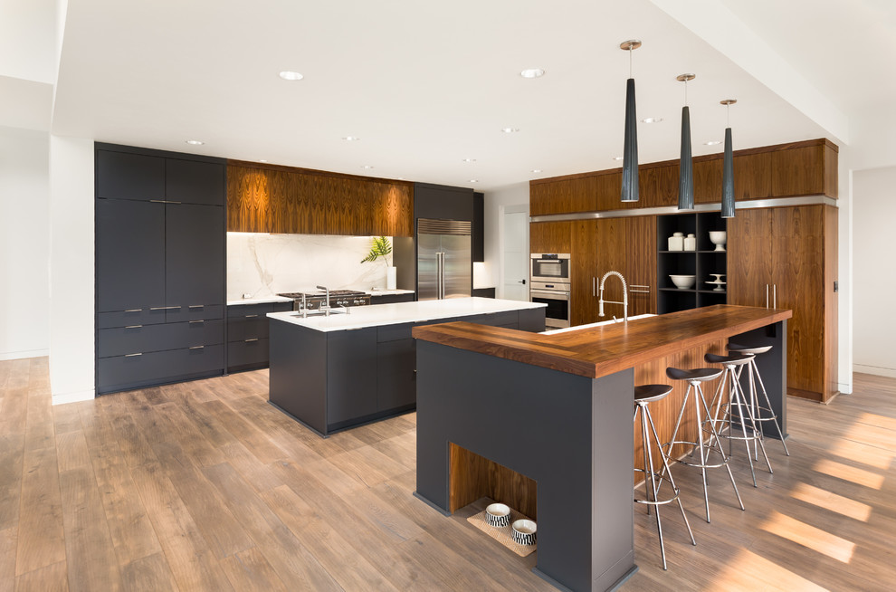 Inspiration for a large modern l-shaped eat-in kitchen in Toronto with an undermount sink, flat-panel cabinets, medium wood cabinets, white splashback, stainless steel appliances, medium hardwood floors, multiple islands, brown floor, white benchtop and stone slab splashback.