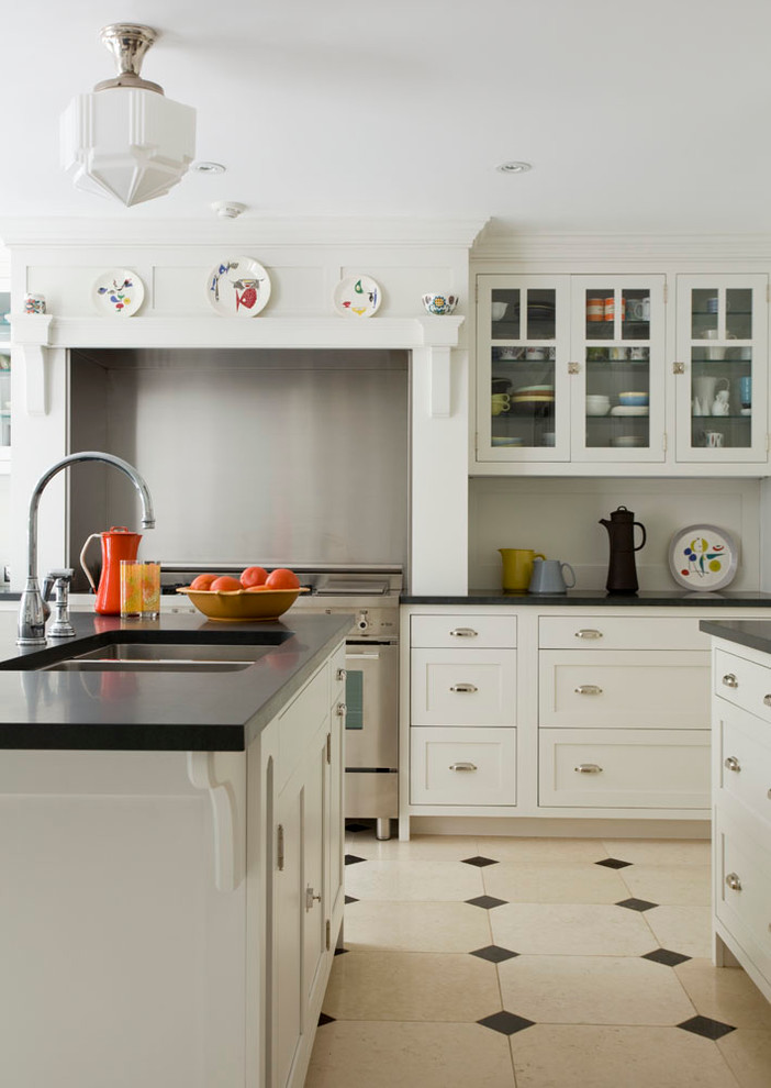 Mid-sized transitional separate kitchen in New York with an undermount sink, glass-front cabinets, white cabinets, soapstone benchtops, white splashback, stainless steel appliances, limestone floors, with island and beige floor.