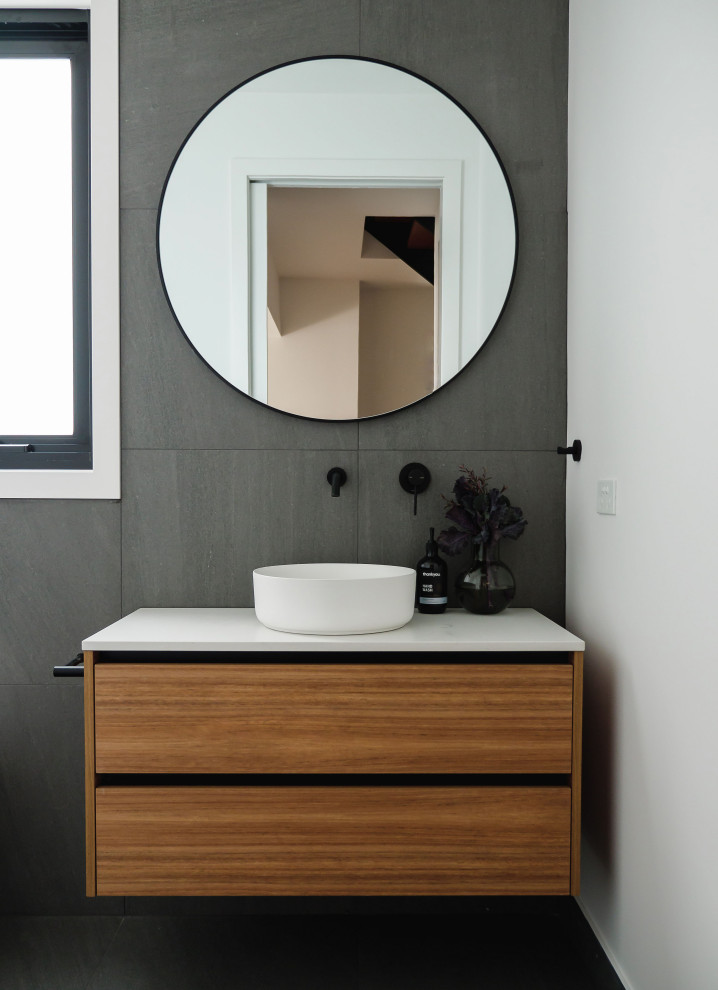 Photo of a contemporary bathroom in Melbourne with flat-panel cabinets, medium wood cabinets, gray tile, grey walls, a vessel sink, grey floor and white benchtops.