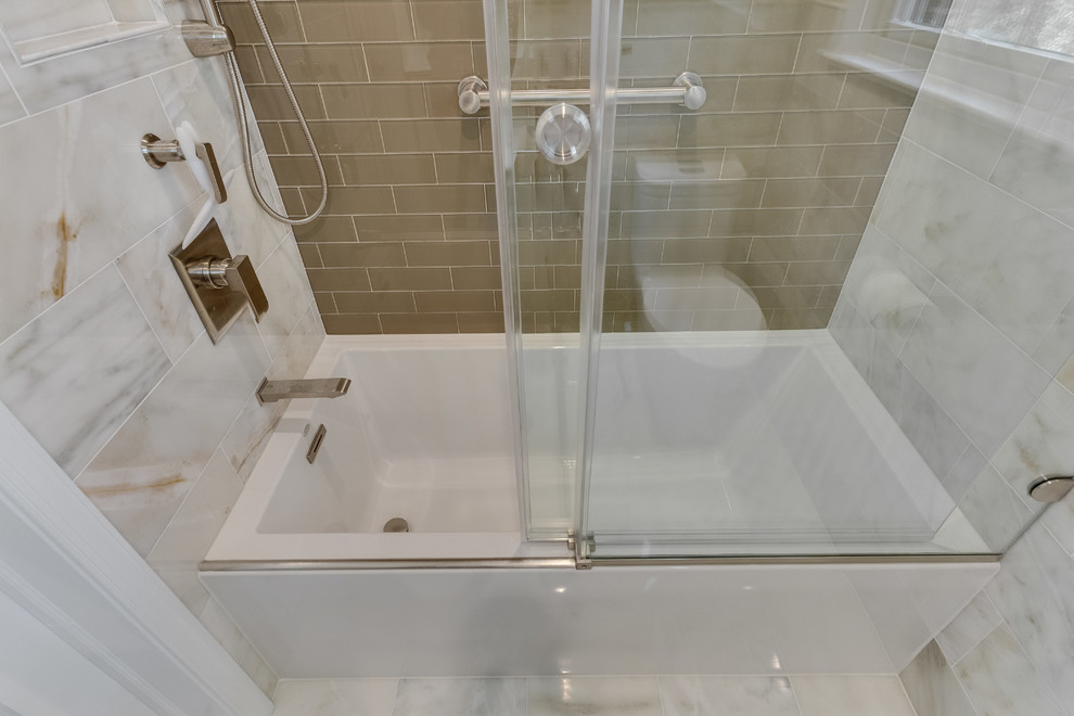 Photo of a mid-sized transitional kids bathroom in DC Metro with flat-panel cabinets, white cabinets, an alcove tub, a shower/bathtub combo, a one-piece toilet, multi-coloured tile, beige walls, marble floors, a wall-mount sink, glass benchtops, multi-coloured floor and a sliding shower screen.