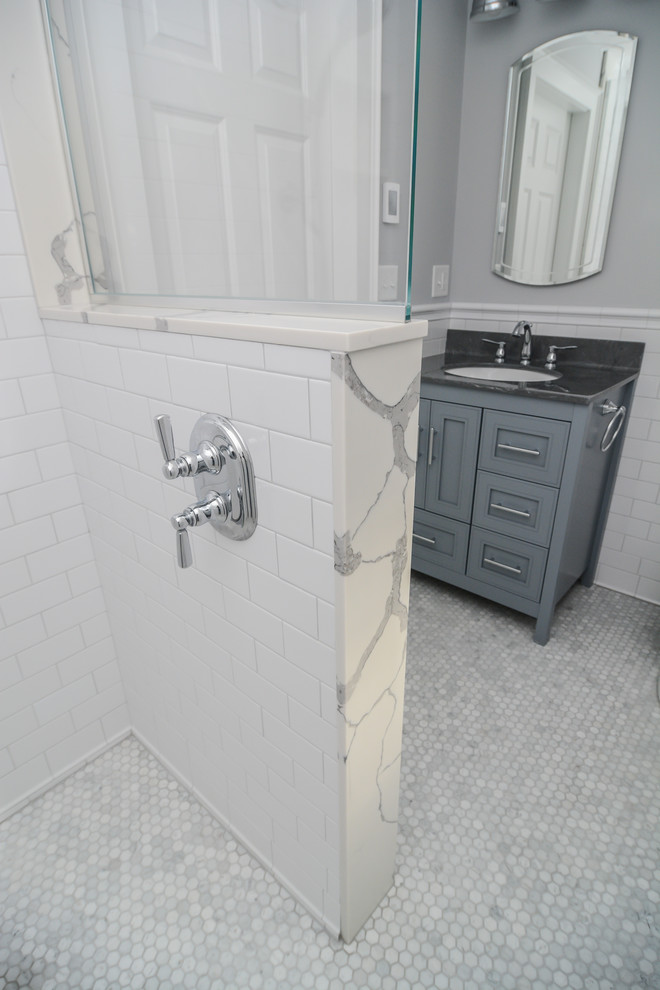 This is an example of a small transitional master bathroom in Boston with recessed-panel cabinets, grey cabinets, a curbless shower, a two-piece toilet, white tile, subway tile, grey walls, marble floors, an undermount sink, solid surface benchtops, grey floor, an open shower and green benchtops.