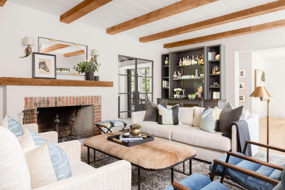 This is an example of a mediterranean open concept living room in San Francisco with white walls, medium hardwood floors, a standard fireplace, a brick fireplace surround, brown floor and exposed beam.