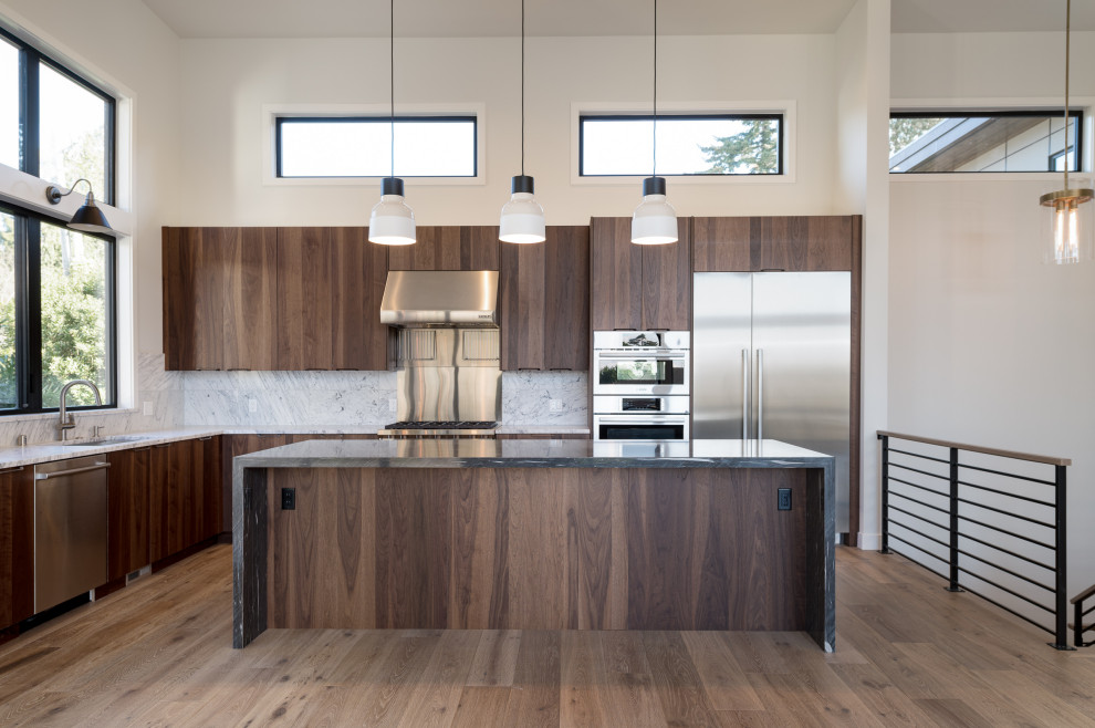 Expansive modern l-shaped open plan kitchen in Phoenix with a double-bowl sink, flat-panel cabinets, dark wood cabinets, granite benchtops, white splashback, granite splashback, stainless steel appliances, light hardwood floors, with island, brown floor and grey benchtop.