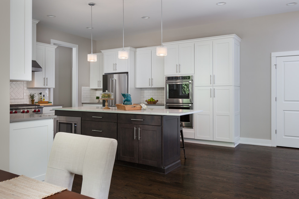 Mid-sized transitional u-shaped dark wood floor and brown floor open concept kitchen photo in Chicago with a farmhouse sink, shaker cabinets, white cabinets, white backsplash, subway tile backsplash, stainless steel appliances, an island, gray countertops and quartz countertops