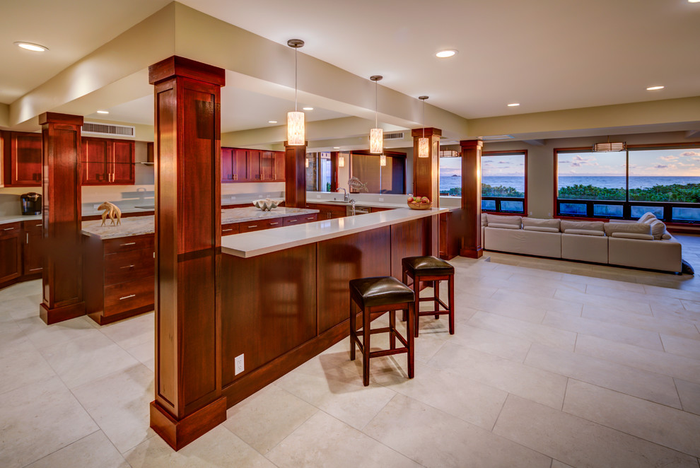This is an example of a large tropical open plan kitchen in Hawaii with an undermount sink, shaker cabinets, medium wood cabinets, solid surface benchtops, stainless steel appliances, limestone floors and multiple islands.