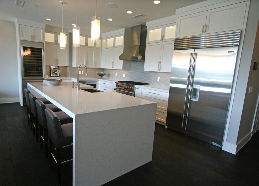 Inspiration for a mid-sized transitional l-shaped dark wood floor open concept kitchen remodel in Seattle with a farmhouse sink, shaker cabinets, white cabinets, quartz countertops, gray backsplash, glass tile backsplash, stainless steel appliances and an island