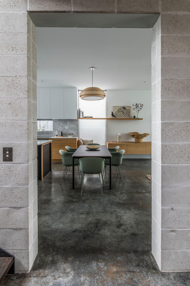 Cette image montre une salle à manger ouverte sur le salon nordique de taille moyenne avec un mur blanc, sol en béton ciré, un sol gris et un mur en parement de brique.