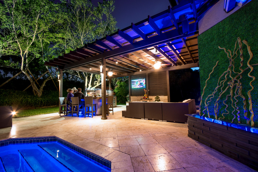 Expansive traditional backyard patio in Miami with an outdoor kitchen, natural stone pavers and a pergola.