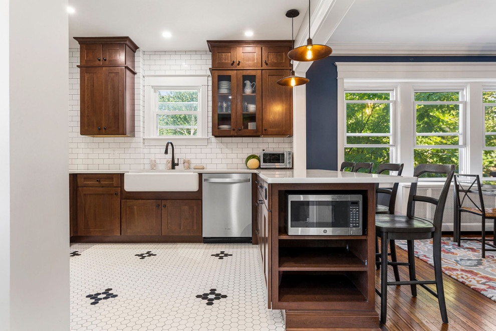 Kitchen - large traditional porcelain tile and white floor kitchen idea in Philadelphia with a farmhouse sink, shaker cabinets, brown cabinets, quartz countertops, white backsplash, subway tile backsplash, stainless steel appliances, a peninsula and white countertops