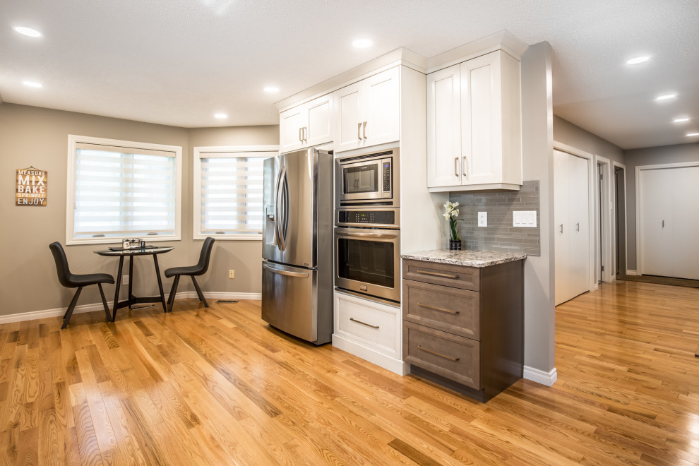 Eat-in kitchen - mid-sized transitional single-wall medium tone wood floor and beige floor eat-in kitchen idea in Edmonton with an undermount sink, shaker cabinets, beige cabinets, granite countertops, beige backsplash, glass tile backsplash, stainless steel appliances, an island and beige countertops