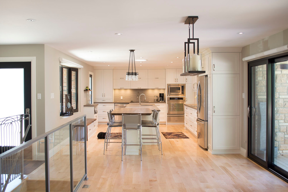 Open concept kitchen - large transitional light wood floor open concept kitchen idea with an undermount sink, shaker cabinets, white cabinets, wood countertops, gray backsplash, porcelain backsplash, stainless steel appliances and an island
