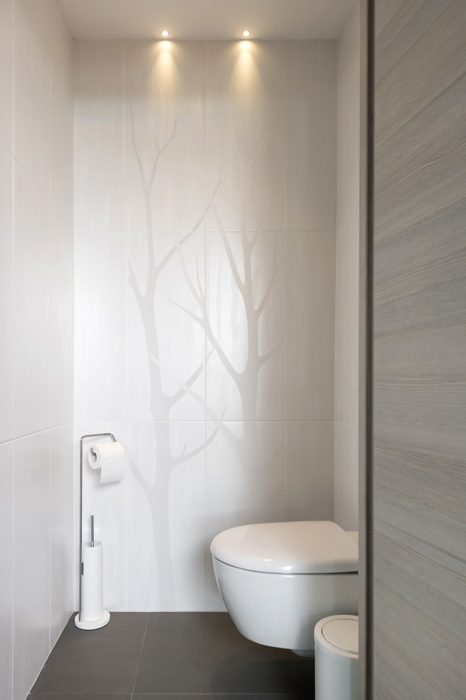 Mid-sized contemporary powder room in Lyon with recessed-panel cabinets, light wood cabinets, a wall-mount toilet, white tile, ceramic tile, white walls and ceramic floors.