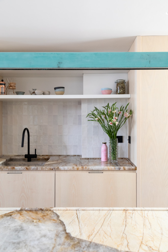Exemple de cuisine ouverte in U and bois clair With un évier intégré, un placard à porte plane, un plan de travail en quartz, une crédence blanche, une crédence en céramique, un électroménager noir, un sol en carrelage de céramique, îlot, un sol beige and un plan de travail beige.