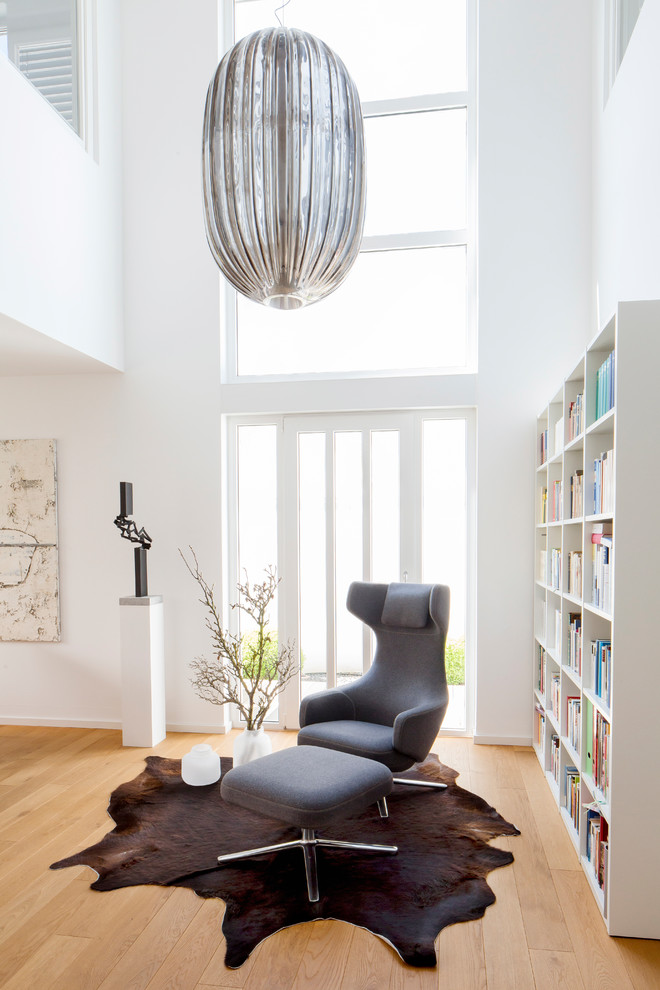 Inspiration for a contemporary living room in Dusseldorf with a library, white walls, light hardwood floors, brown floor and no fireplace.