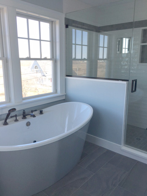 This is an example of a large beach style master bathroom in Providence with a freestanding tub, a one-piece toilet, ceramic floors, an integrated sink, marble benchtops, grey floor, glass tile, a hinged shower door and blue walls.