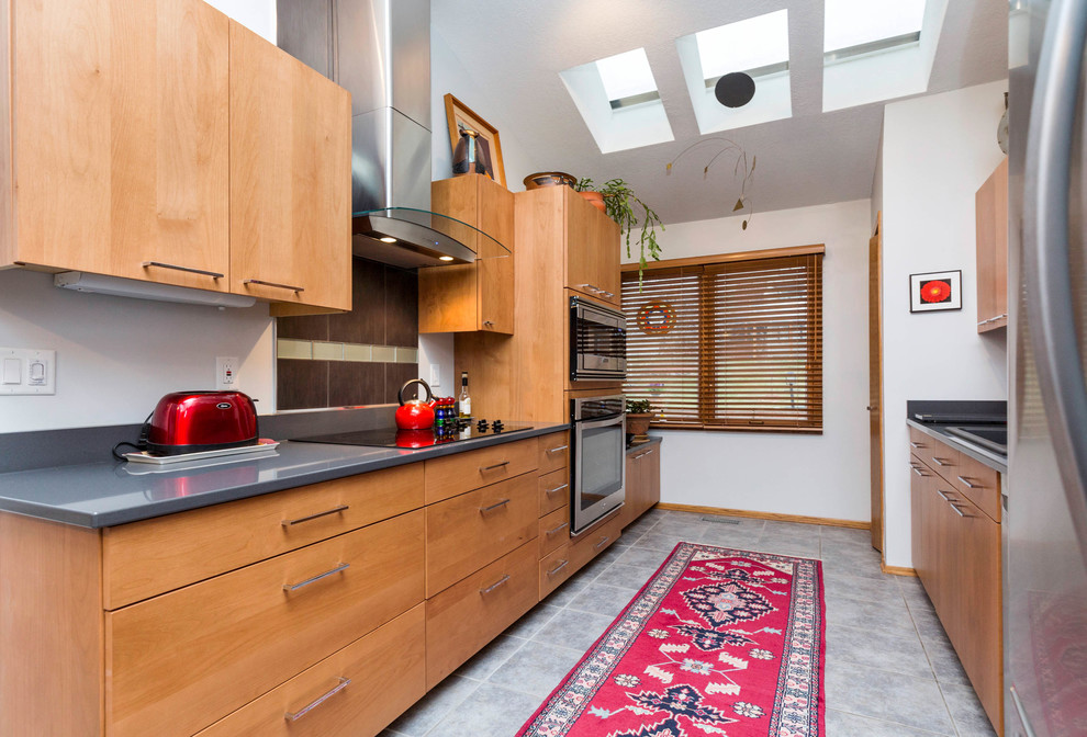 Photo of a large modern galley eat-in kitchen in Other with a drop-in sink, flat-panel cabinets, light wood cabinets, soapstone benchtops, grey splashback, stone tile splashback, stainless steel appliances, porcelain floors, a peninsula and grey floor.