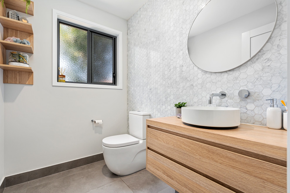 Design ideas for a mid-sized modern kids bathroom in Gold Coast - Tweed with flat-panel cabinets, light wood cabinets, a one-piece toilet, gray tile, mosaic tile, grey walls, porcelain floors, a vessel sink, wood benchtops and grey floor.