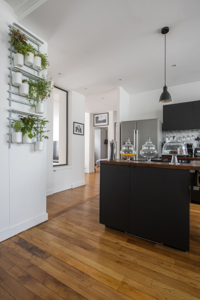Design ideas for a mid-sized contemporary galley open plan kitchen in Paris with an undermount sink, flat-panel cabinets, black cabinets, wood benchtops, white splashback, timber splashback, stainless steel appliances, medium hardwood floors, multiple islands, brown floor and brown benchtop.