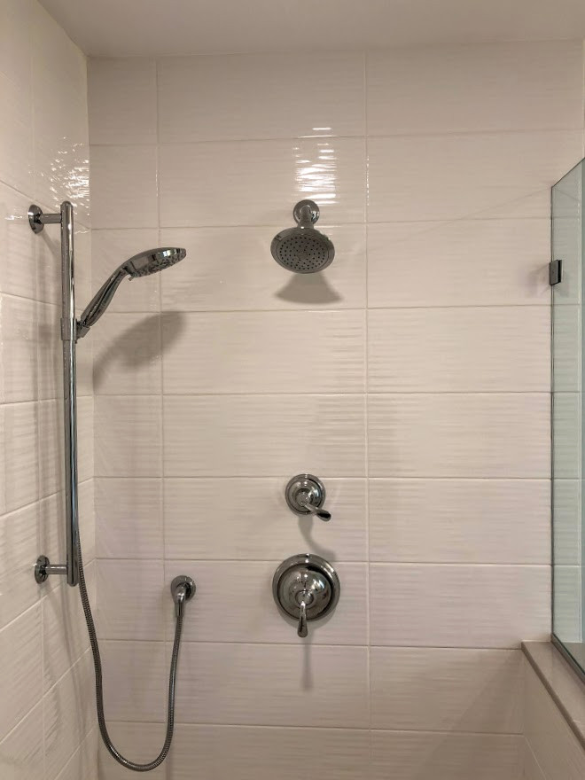 This is an example of a medium sized traditional ensuite bathroom in Baltimore with shaker cabinets, white cabinets, a walk-in shower, a one-piece toilet, white tiles, ceramic tiles, grey walls, porcelain flooring, a submerged sink, engineered stone worktops, brown floors, an open shower, grey worktops, a shower bench, double sinks and a freestanding vanity unit.