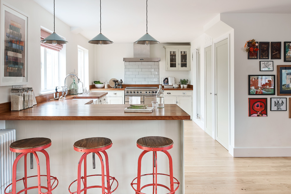 Inspiration for a country u-shaped kitchen in Wiltshire with a farmhouse sink, shaker cabinets, white cabinets, wood benchtops, white splashback, stainless steel appliances, light hardwood floors, a peninsula, beige floor and brown benchtop.