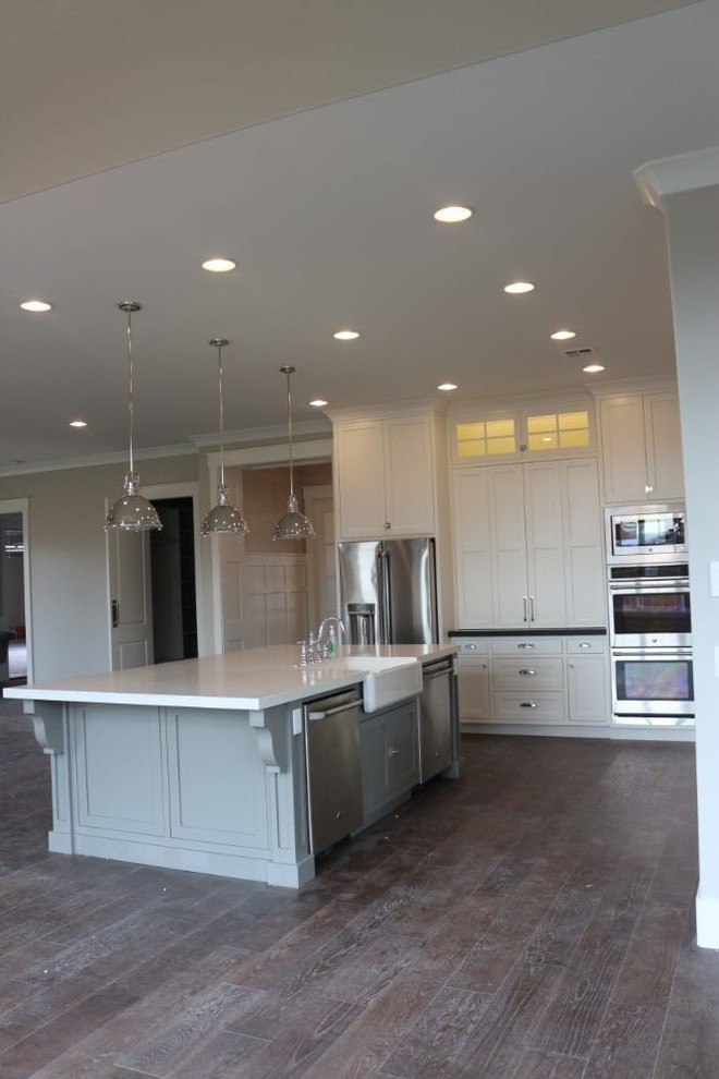Inspiration for a large transitional l-shaped open plan kitchen in Salt Lake City with shaker cabinets, white cabinets, with island, a farmhouse sink, quartz benchtops, stainless steel appliances, dark hardwood floors, brown floor and white benchtop.
