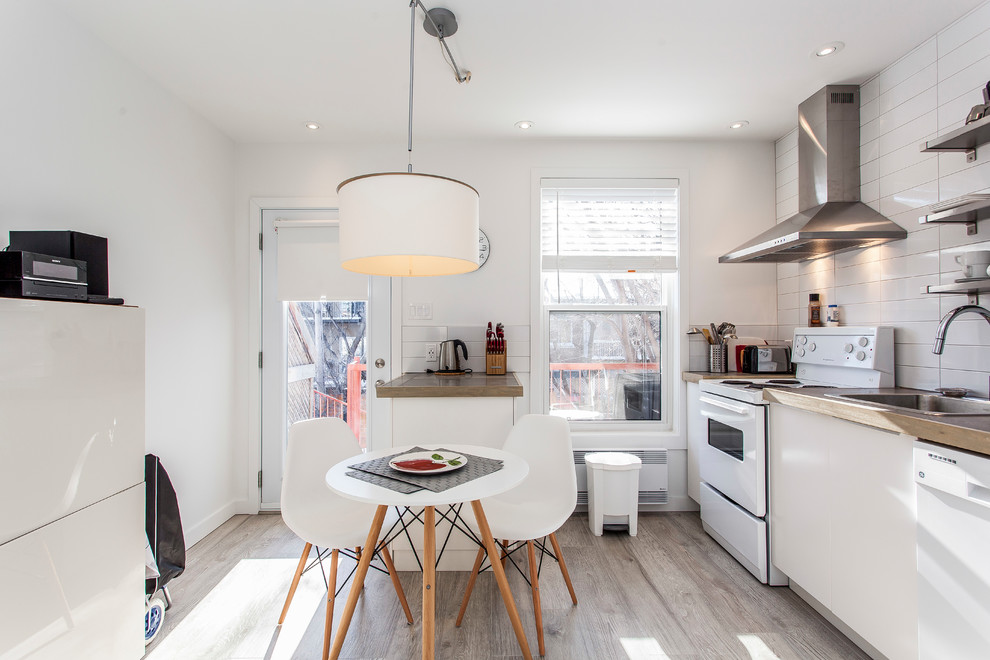 Scandinavian single-wall kitchen in Montreal with a drop-in sink, flat-panel cabinets, white cabinets, wood benchtops, white splashback, white appliances and no island.