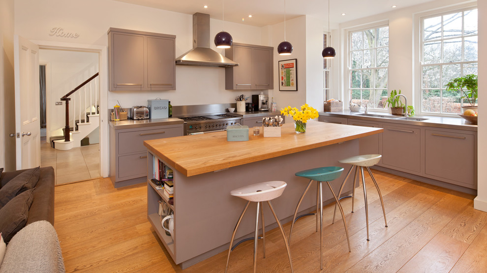 Photo of a transitional l-shaped kitchen in Oxfordshire with flat-panel cabinets, grey cabinets, wood benchtops, stainless steel appliances, medium hardwood floors, with island and an integrated sink.