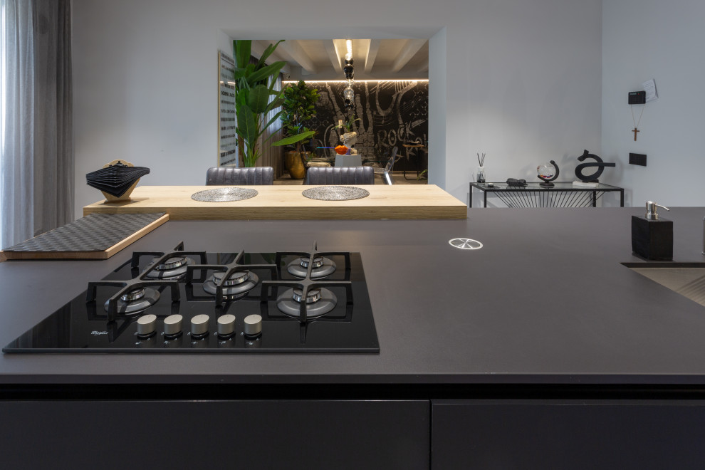 Photo of a contemporary u-shaped kitchen in Other with a drop-in sink, flat-panel cabinets, black cabinets, black appliances and black benchtop.