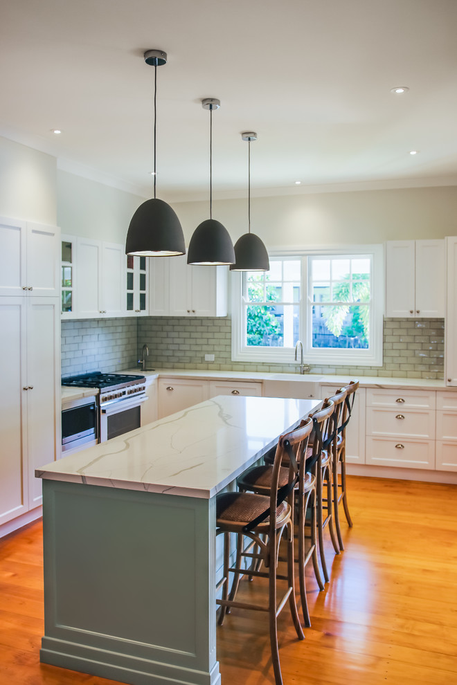 Large traditional l-shaped eat-in kitchen in Brisbane with a farmhouse sink, shaker cabinets, green cabinets, quartz benchtops, green splashback, subway tile splashback, white appliances, medium hardwood floors, with island and green benchtop.