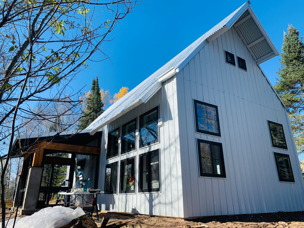 На фото: маленький, двухэтажный, белый мини дом в стиле кантри с облицовкой из металла, двускатной крышей и металлической крышей для на участке и в саду с
