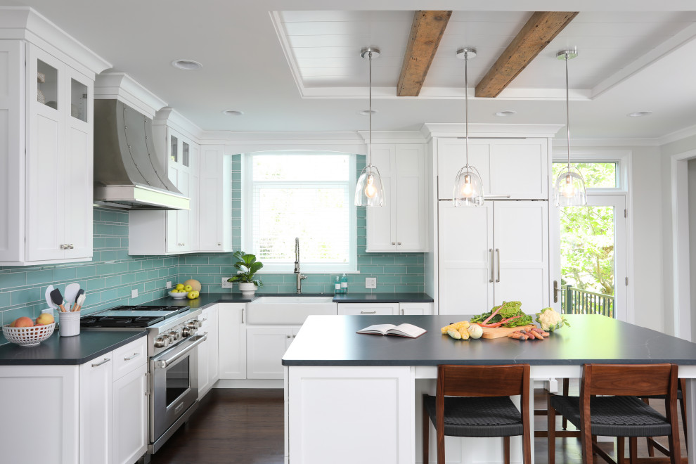 Inspiration for a large transitional l-shaped eat-in kitchen in Chicago with a farmhouse sink, white cabinets, soapstone benchtops, blue splashback, glass tile splashback, panelled appliances, dark hardwood floors, with island, brown floor, black benchtop and shaker cabinets.