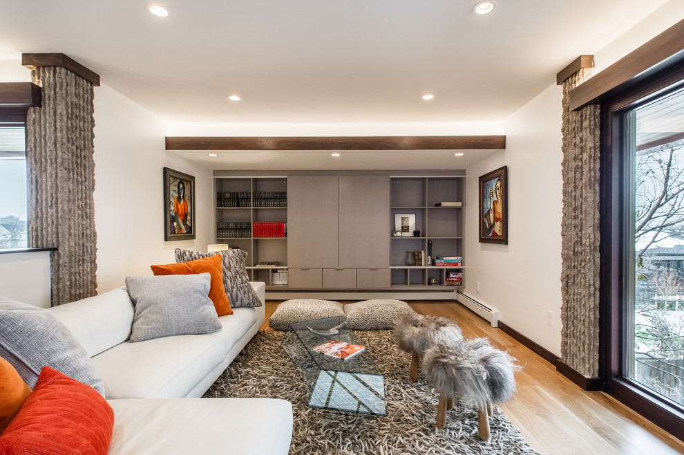 This is an example of a large contemporary family room in Denver with white walls, light hardwood floors and a concealed tv.
