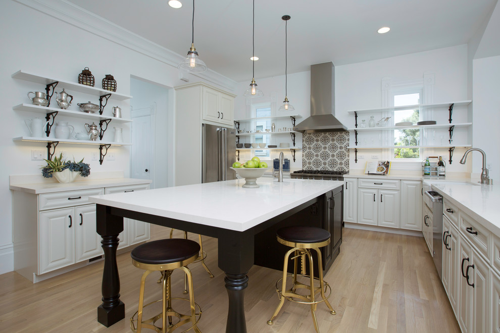 This is an example of a mid-sized transitional u-shaped kitchen in San Francisco with a farmhouse sink, raised-panel cabinets, white cabinets, limestone benchtops, white splashback, stainless steel appliances, light hardwood floors, with island and beige floor.