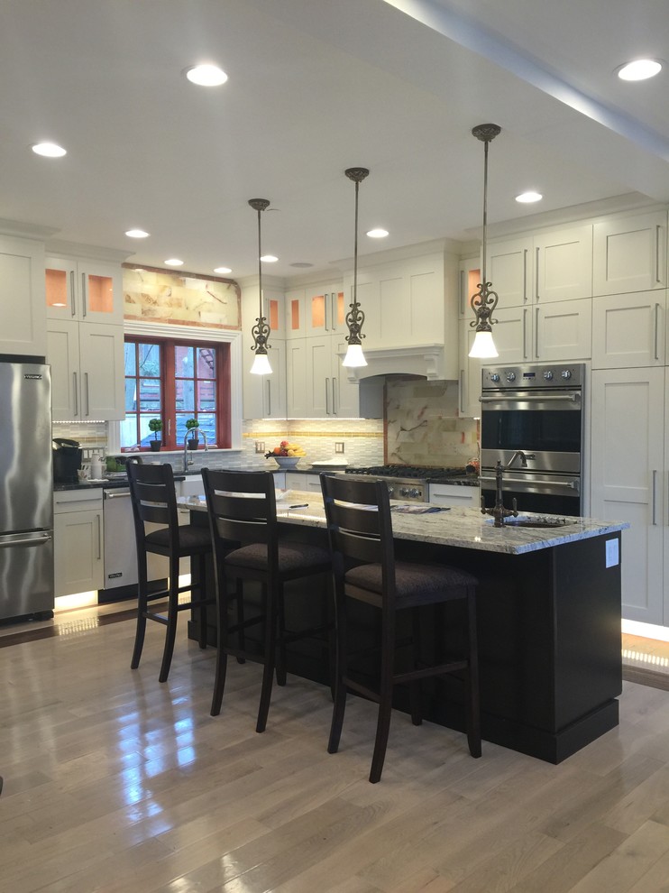 Eat-in kitchen - mid-sized transitional u-shaped light wood floor and beige floor eat-in kitchen idea in Boston with recessed-panel cabinets, white cabinets, stainless steel appliances, an island, a farmhouse sink, granite countertops, beige backsplash, stone tile backsplash and multicolored countertops