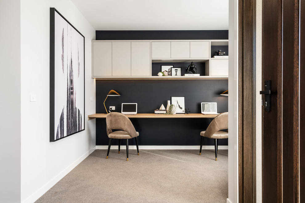 This is an example of a contemporary home office in Melbourne with black walls, carpet, a built-in desk and beige floor.