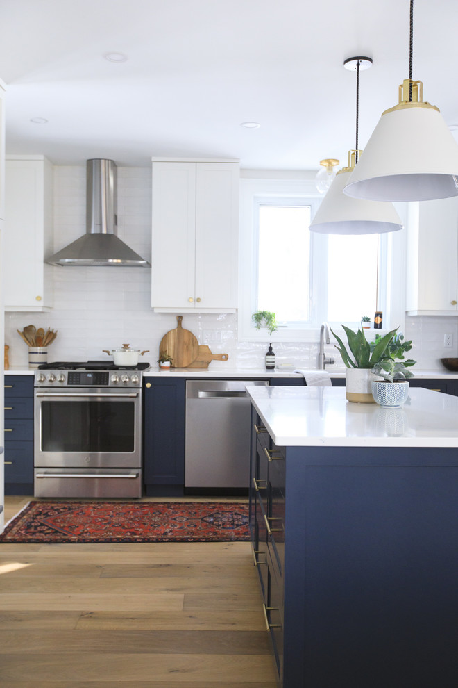 Photo of a mid-sized transitional u-shaped eat-in kitchen in Toronto with an undermount sink, shaker cabinets, blue cabinets, quartz benchtops, white splashback, subway tile splashback, stainless steel appliances, light hardwood floors, with island, beige floor and white benchtop.