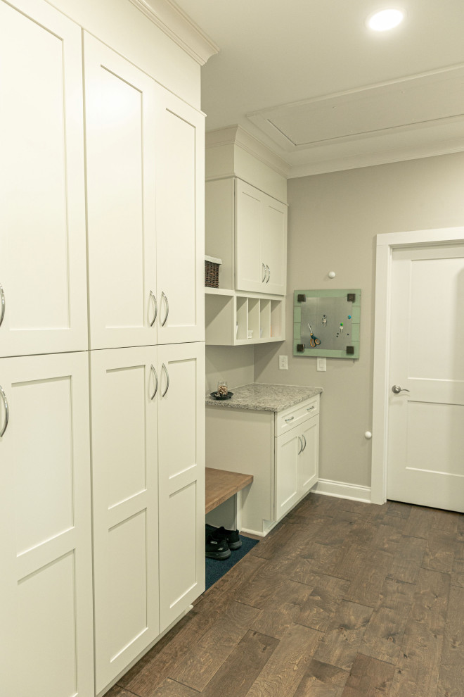 Inspiration for a mid-sized transitional single-wall utility room in Other with flat-panel cabinets, white cabinets, quartz benchtops, beige walls, medium hardwood floors, a concealed washer and dryer, brown floor and grey benchtop.