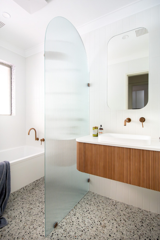 Foto på ett vit badrum, med släta luckor, skåp i mellenmörkt trä, ett badkar i en alkov, en kantlös dusch, vit kakel, ett fristående handfat, grått golv och med dusch som är öppen