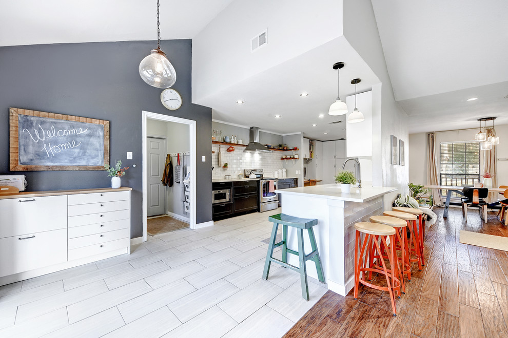 Example of a transitional u-shaped gray floor open concept kitchen design in Austin with an undermount sink, flat-panel cabinets, black cabinets, white backsplash, subway tile backsplash, stainless steel appliances and a peninsula