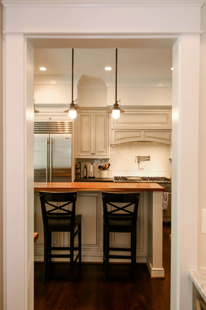 Large traditional l-shaped eat-in kitchen in DC Metro with raised-panel cabinets, beige cabinets, wood benchtops, beige splashback, subway tile splashback, stainless steel appliances, dark hardwood floors, with island and a farmhouse sink.