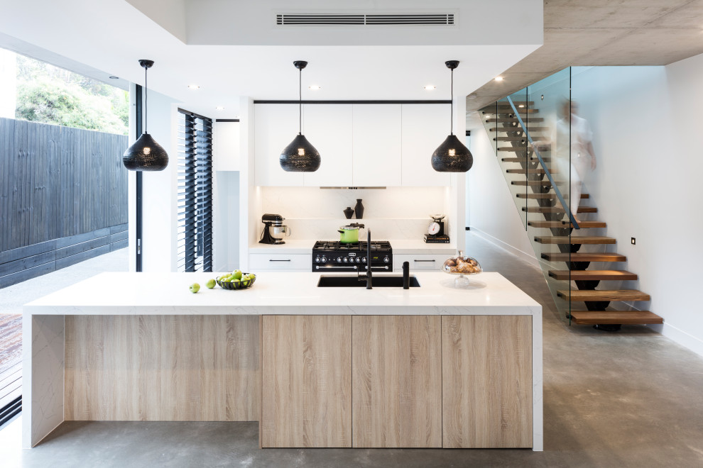 Inspiration for a contemporary galley kitchen with an undermount sink, flat-panel cabinets, white cabinets, white splashback, black appliances, concrete floors, with island, grey floor and white benchtop.