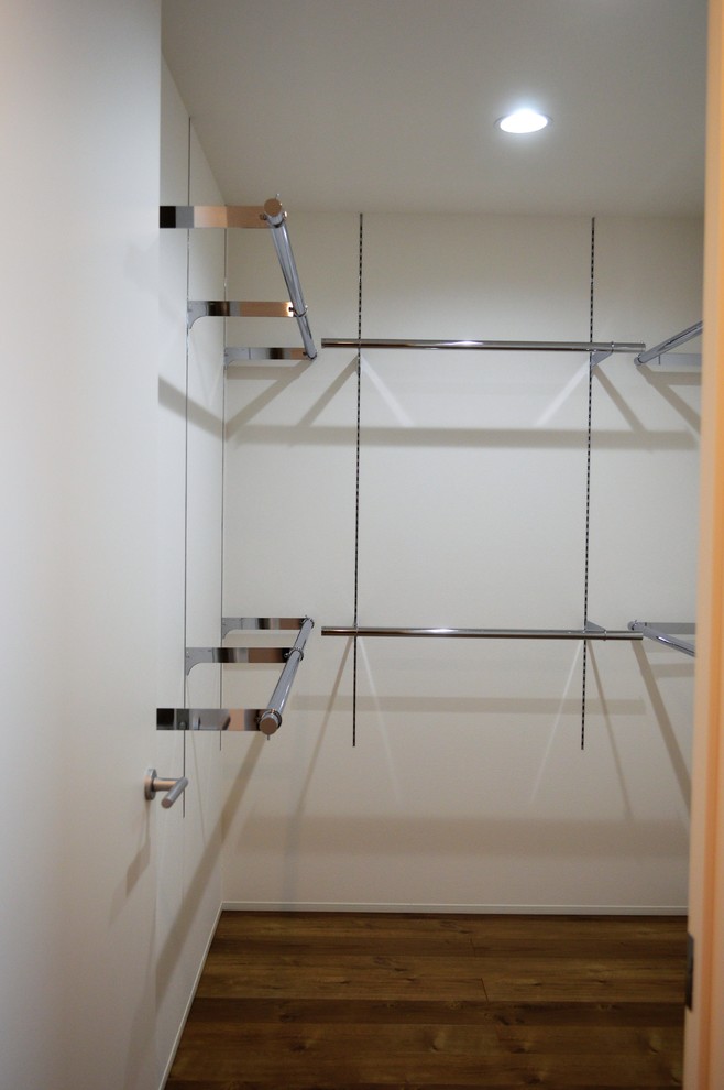 Inredning av ett 50 tals mellanstort walk-in-closet för könsneutrala, med luckor med profilerade fronter, vita skåp, plywoodgolv och brunt golv